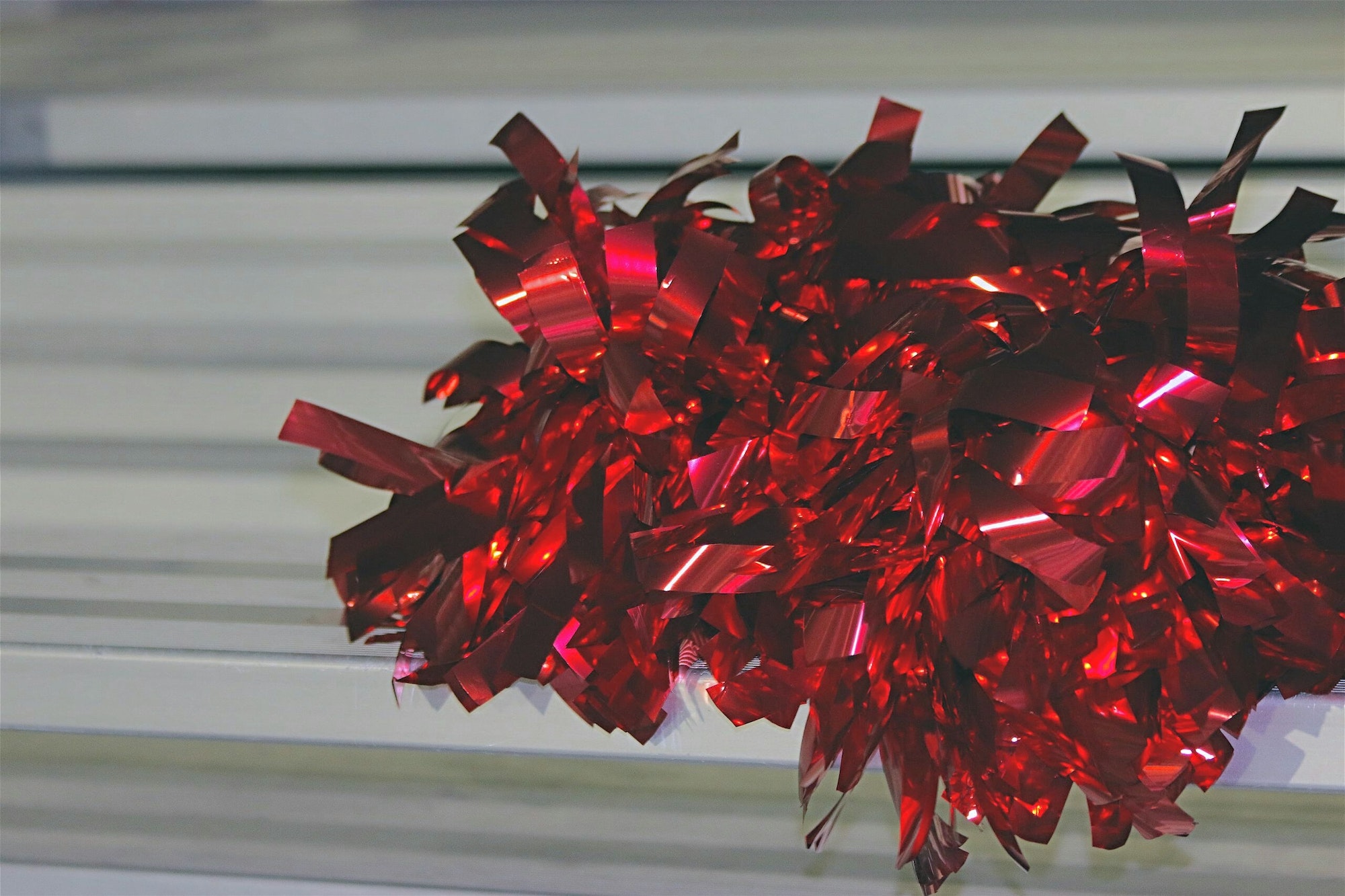Minimalist image of bright red metallic cheerleading pom pom on football stadium seat.