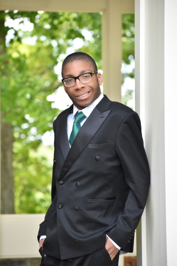 Senior photo of student smiling, wearing tuxedo and green tie outside