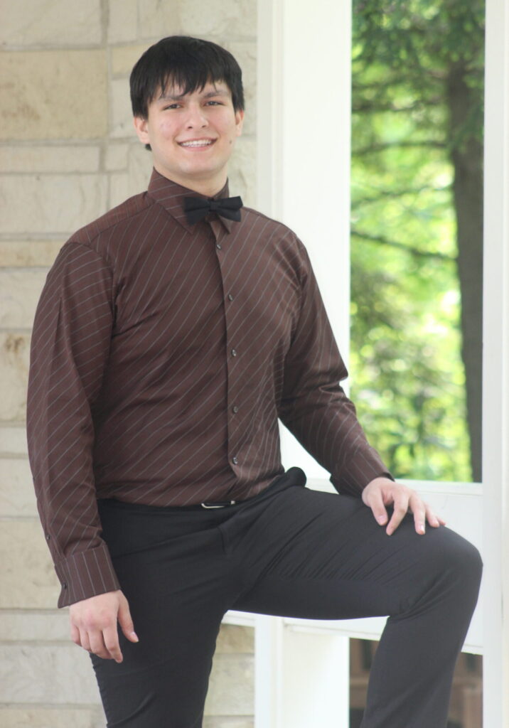 Student smiling for his senior photos outside wearing brown button down shirt and dress pants