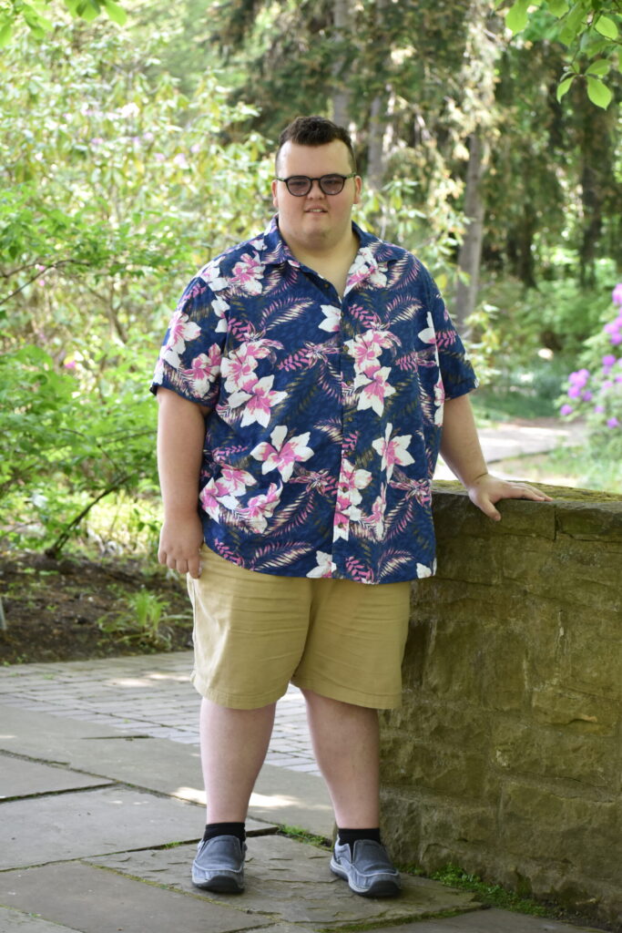 PD student graduation photo, smiling outside with hawaiian shirt and khaki shorts on